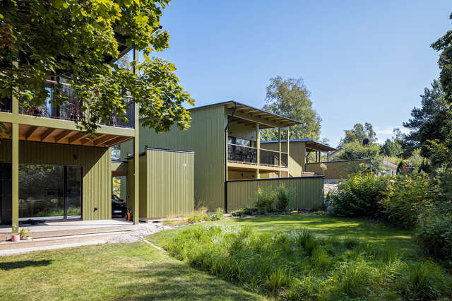 A grass yard with a green wooden house in the background.