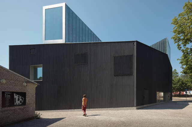 Dark-coloured box-like wooden building with a skylight protruding from the roof