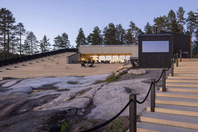 Waterfront with rocks in foreground and large wooden structure with staircase in background.