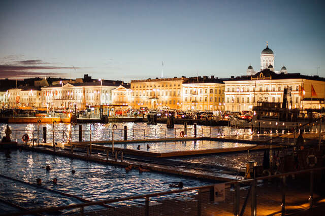 Sea pool with the market square and an illuminated city shoreline in the background.