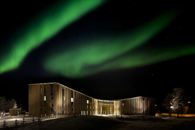 Lighted building with wooden facades in a dark night, northern lights blazing above.