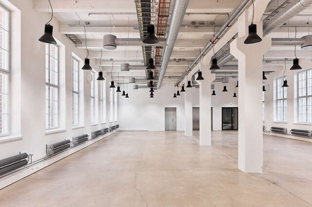 Large room with black lamps hanging from ceiling and windows on both walls. Large white pillars in center of the large room.