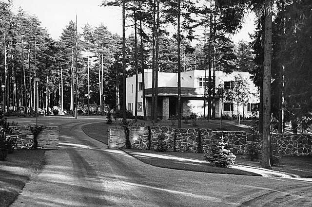 Black and white picture of a white two storey building behind some trees.