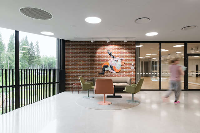 A group of chairs in front of a small brick wall inside a large building. Natural lighting from a large window on the left.