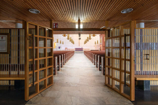 Doors open, view from low space with a wood-lined ceiling towards a high space.