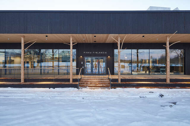 Small patch of snow followed by wooden stairs and a large glass door into a wooden building.