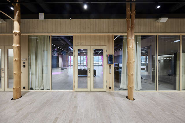 Interior of wooden building. Two large wooden pillars can be seen alongside a glass wall with a doorway.