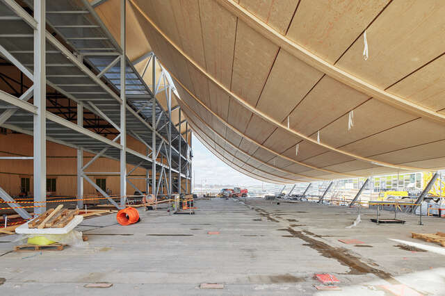 Lobby of the building under construction. Large wooden curvature in the foreground.