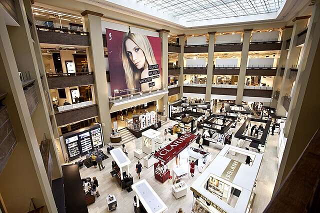 Atrium with cream colored walls and brown railings filled with make up stands.