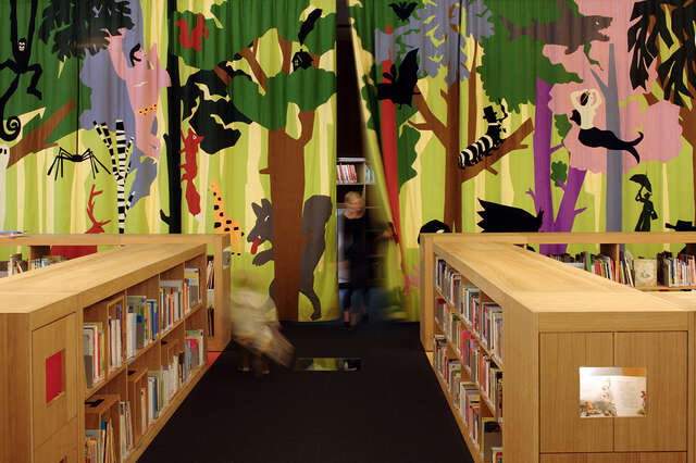 Children's library section with small bookshelves and a curtain with a jungle motive.