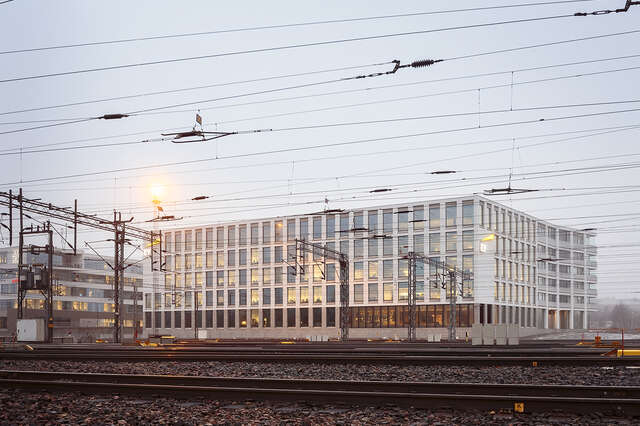 Back of the building with large windows viewed from the traintracks in front of it.