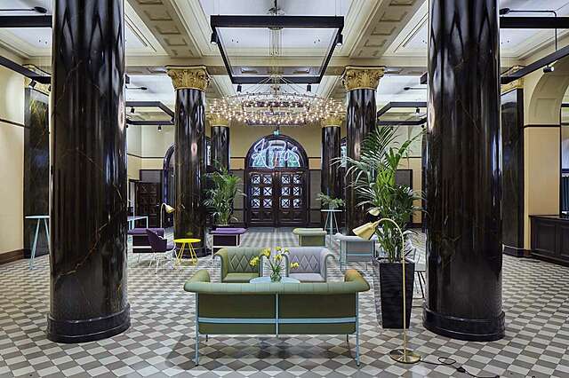 ENtrance lobby with black marble columns, a checkered tile floor, cream colored walls and green and purple furniture.