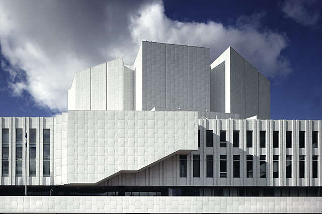 White stone facade of the Finlandia Hall with two rows of windows an d a complex structure at the top of the building.