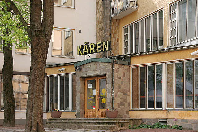 Yellow building with a small protruding stone entrance next to large old windows, above the entrance is the name kåren.