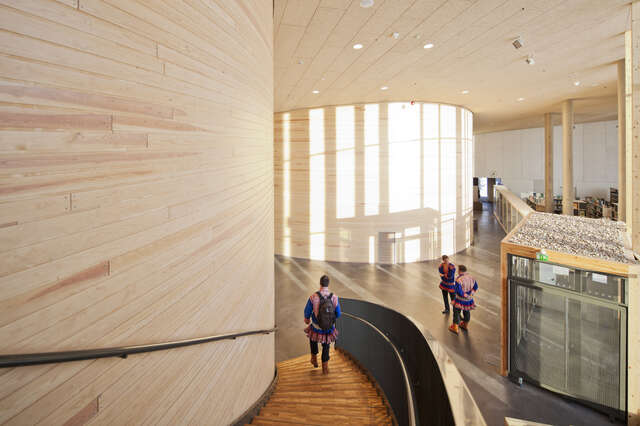 Light, wooden, curved walls and stairs with people walking around in the space.