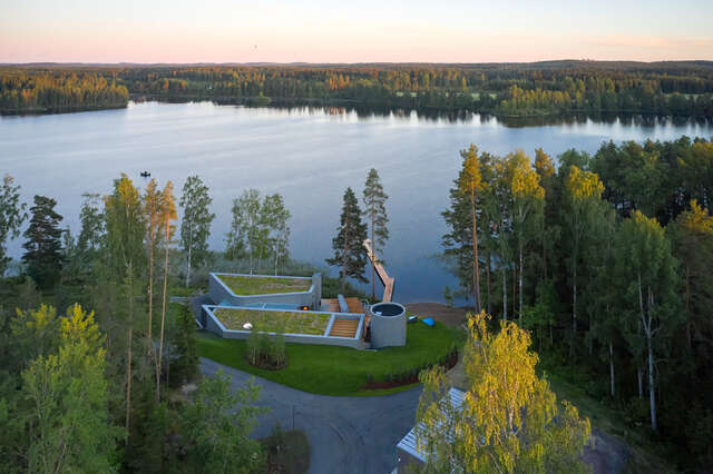 Aerial view of the art sauna with green roofs by a lake.