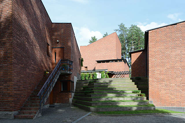In the middle of red-brick buildings there is a staircase covered with grass that is supported by wooden beams.