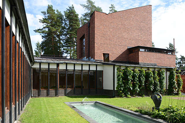 Lawn with an artificial pond, the window front is partly covered by black beams and at the right side the building has a second storey with a tilted roof.