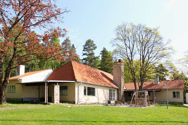 Yellow one storey building with a red roof and a sitting area outside.