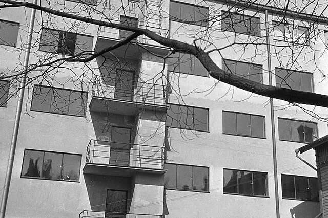 Black and white picture if a bare apartment building with three part windows.