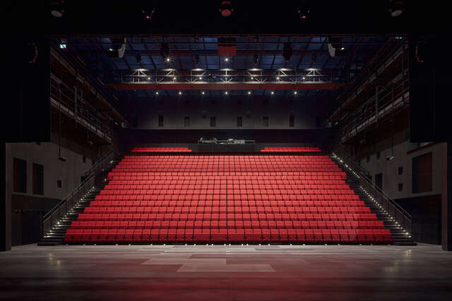 Large red seating area for watching plays. Multiple rows of red seats from wall to wall.