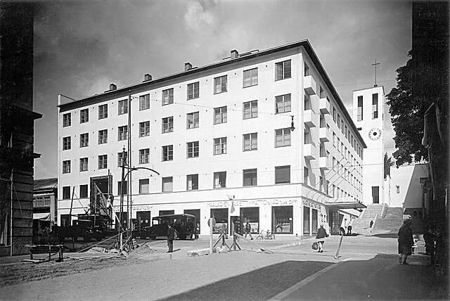 White building with grid windows and shops on the first floor.
