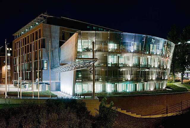 Brick building with a circular wing with glass walls illuminated in the evening.