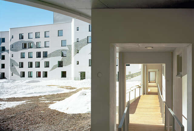 View to a wooden floow corridor and courtyard of a white façade with mosaic details