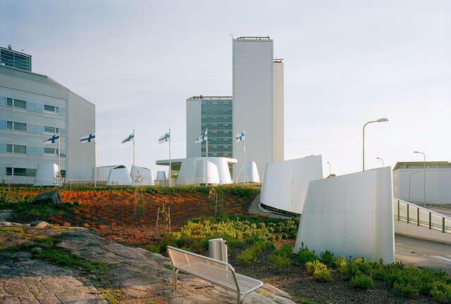 Various white round-shaped and high buildings, park landscape and Finnish flags in flagpoles