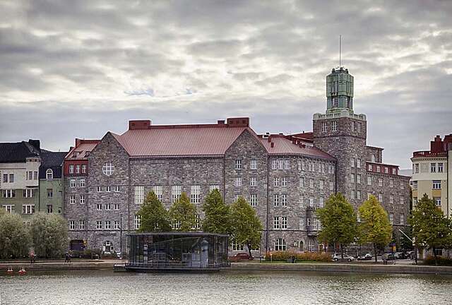 Old stone building, in the from there is a small glass building on the shore.