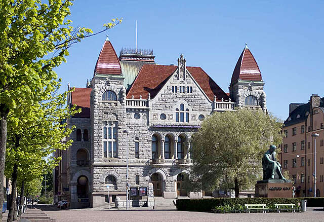 Stone facade with a brown roof and small tower on the sides.