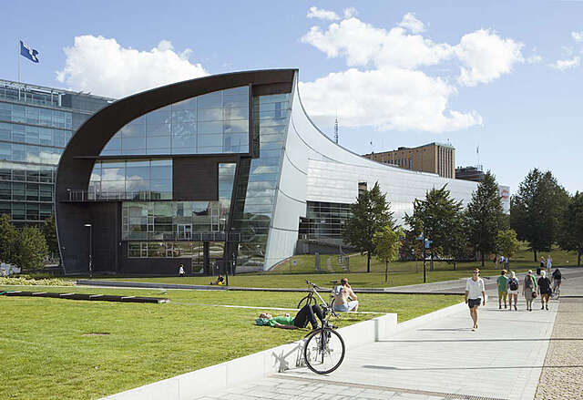 Wave like building with mirrored glass wall next to a public green area.