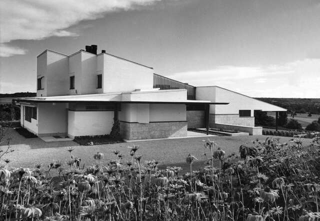White two-storey villa with a lean-to roof, big flower bed in the foreground