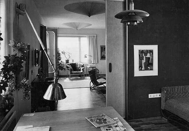 Black and white image of the living room with houseplants, many lamps and armchairs.