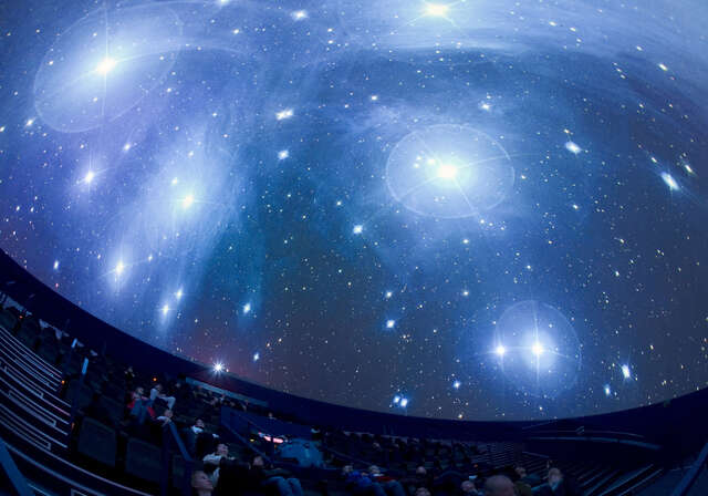 people laying back in their seats and looking at the ceiling with a projection of the sky.
