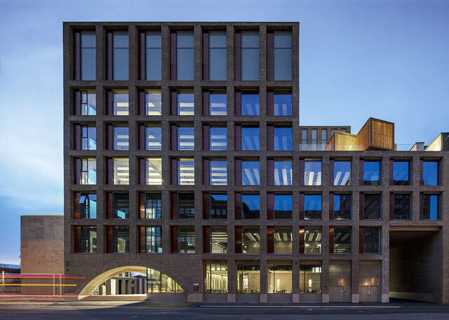 Brown brick facade, large square windows in a grid, some box-like pavilions on the roof