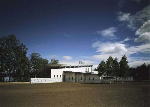 Complex shaped building at the back of a bare field.
