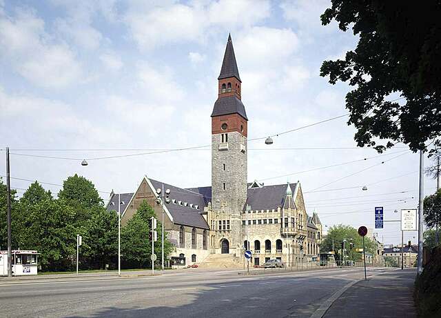 National-romantic buildling with a tall tower next to a paved street