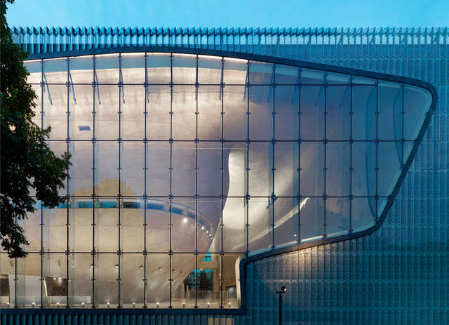 Detail of glass and copper panel façade viewing to the illuminated interiors