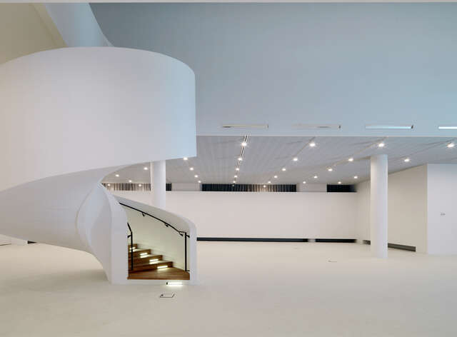 White, curve staircase rising up from a box-like lobby space
