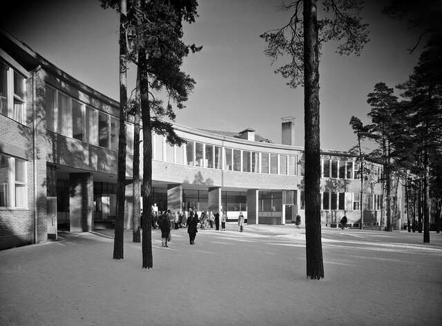 School building in the winter, pinetrees in front of it, children playing