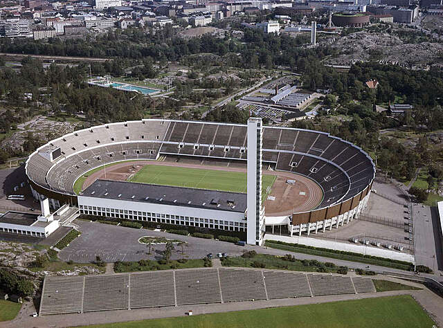 Aerial view of the oval stadium and tower with green and residential surroundings