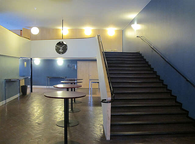 Lobby with four round standing tables with black stairs on the right, the blue walls give the room a retro feeling.