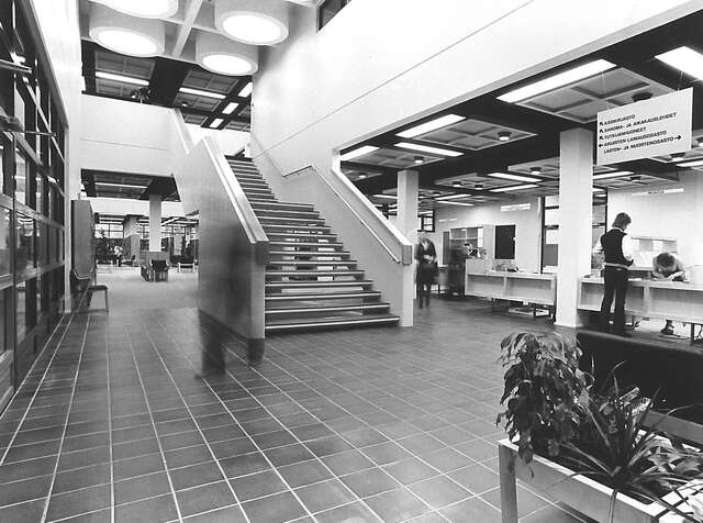 Black and white picture of the staircase with white railings, a tile floor and the information desk.