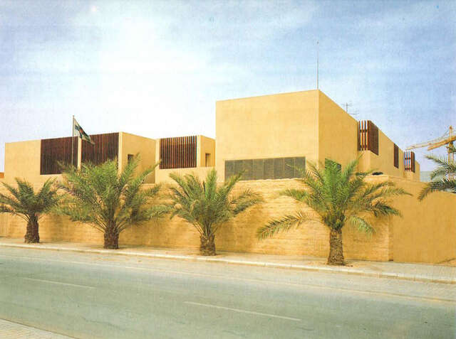 View from the residential street, palm trees and a building on the opposite side of the street.