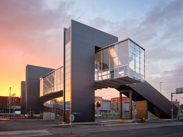 A large glass and metal bridge as seen from street level during sunset