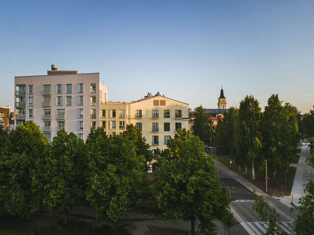 Two large apartment buildings can be seen behind lush green tress during sunset.