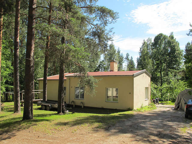 Simple yellow house with a red roof surrounded by trees.