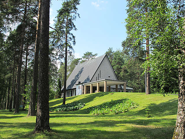 Modern stone building with a triangular black roof and a covered entrance supported by stone pillars.