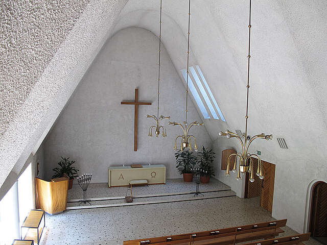 View of the altar of a chapel with whitey plastered walls, a curved ceiling and dark wooden furniture.